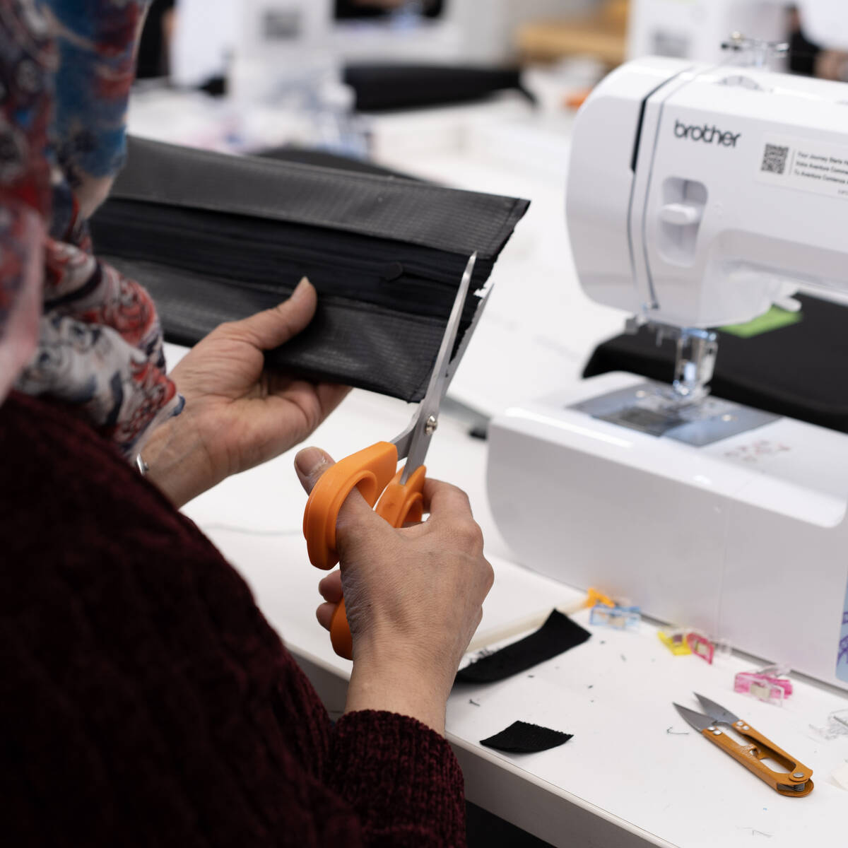 Immigrant woman using scissors to cut material with a sewing machine in the background