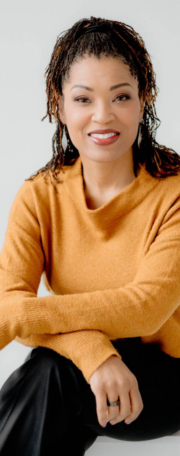 Person sittings with arms crossed, smiling, wearing professional attire and looking directly at the camera.