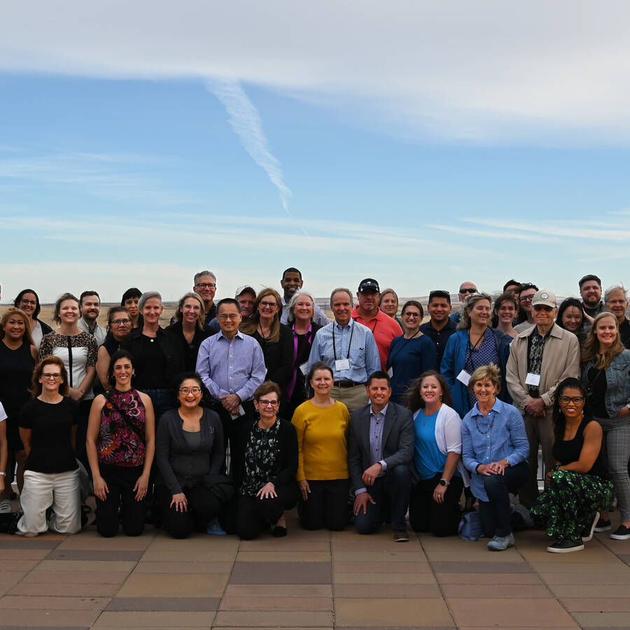 Group of people standing and kneeling in an outdoor area against a blue clear sky.