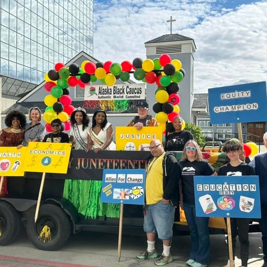 Six people standing in a parade float that says, "Juneteenth" on it while four people stand outside the float, smiling and holding signs with positive messages.
