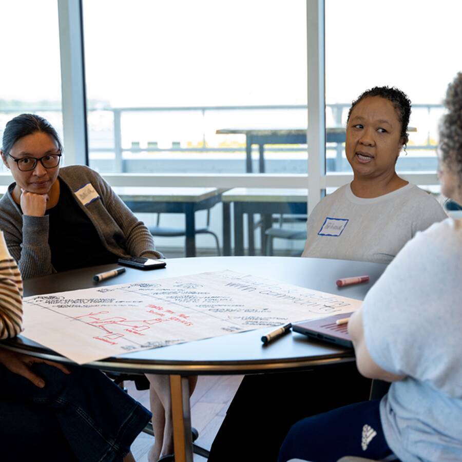 Four people sitting around a table wearing nametags on their shirts, thinking and writing on a large piece of paper