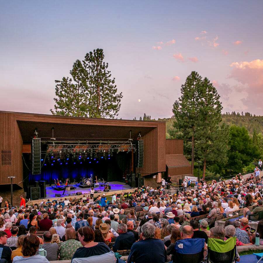 Britt festival outdoor amphitheater with a seated crowd under a blue and pink sunset.