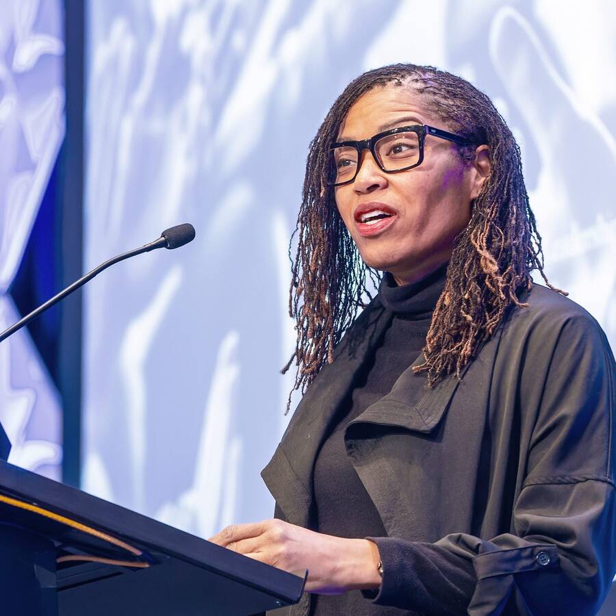 Person speaking on stage behind a podium with a microphone.