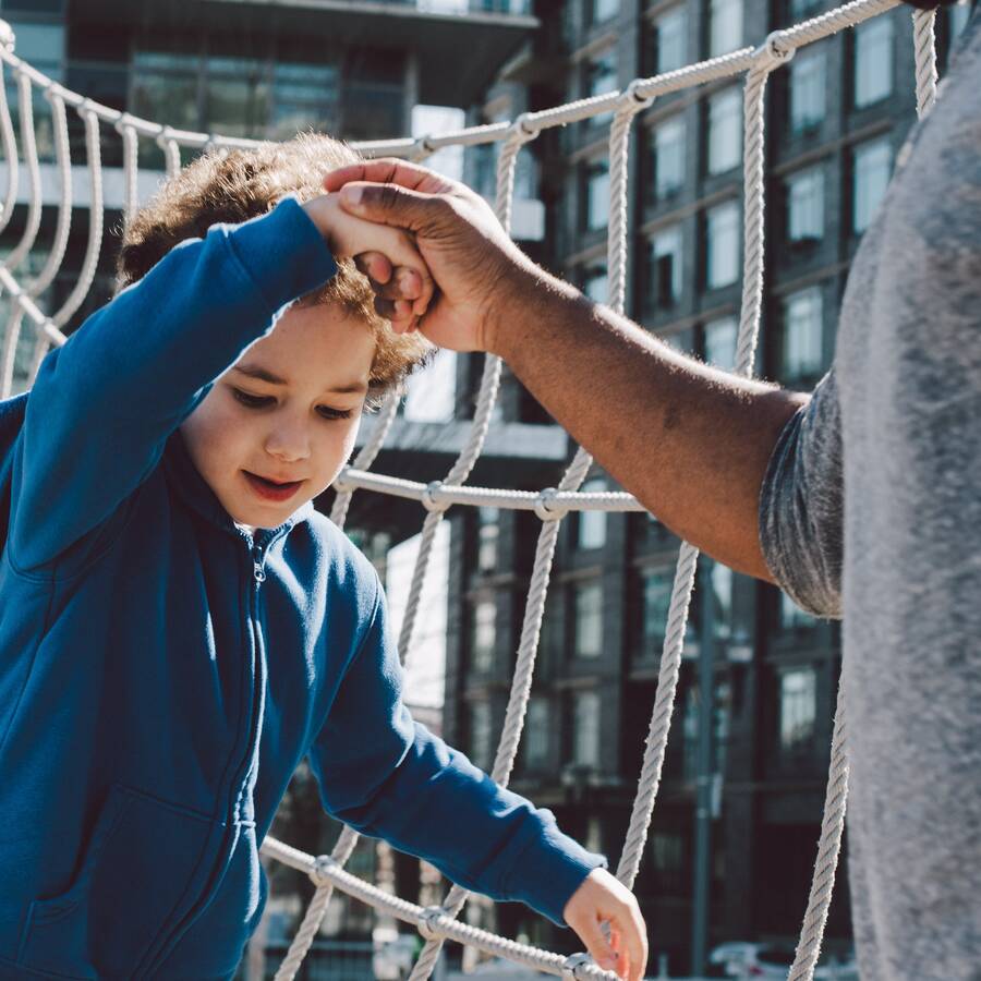 Child in blue sweatshirt walking across something, holding the hand of an adult.