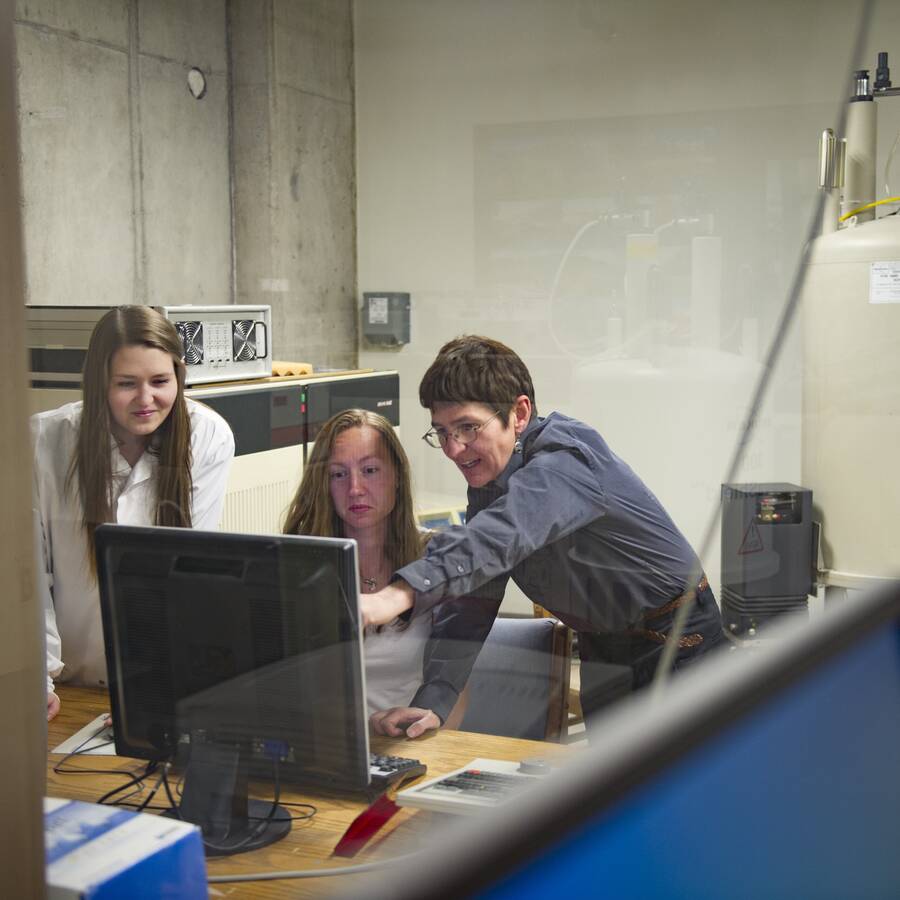 Two Montana State University students learning from a professor, engaged and looking at a computer screen