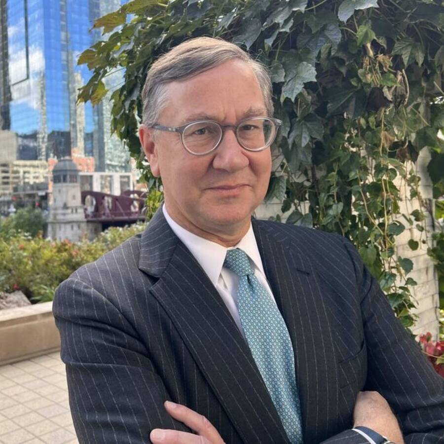 Headshot of person wearing a suit, tie, and glasses and folding their arms.