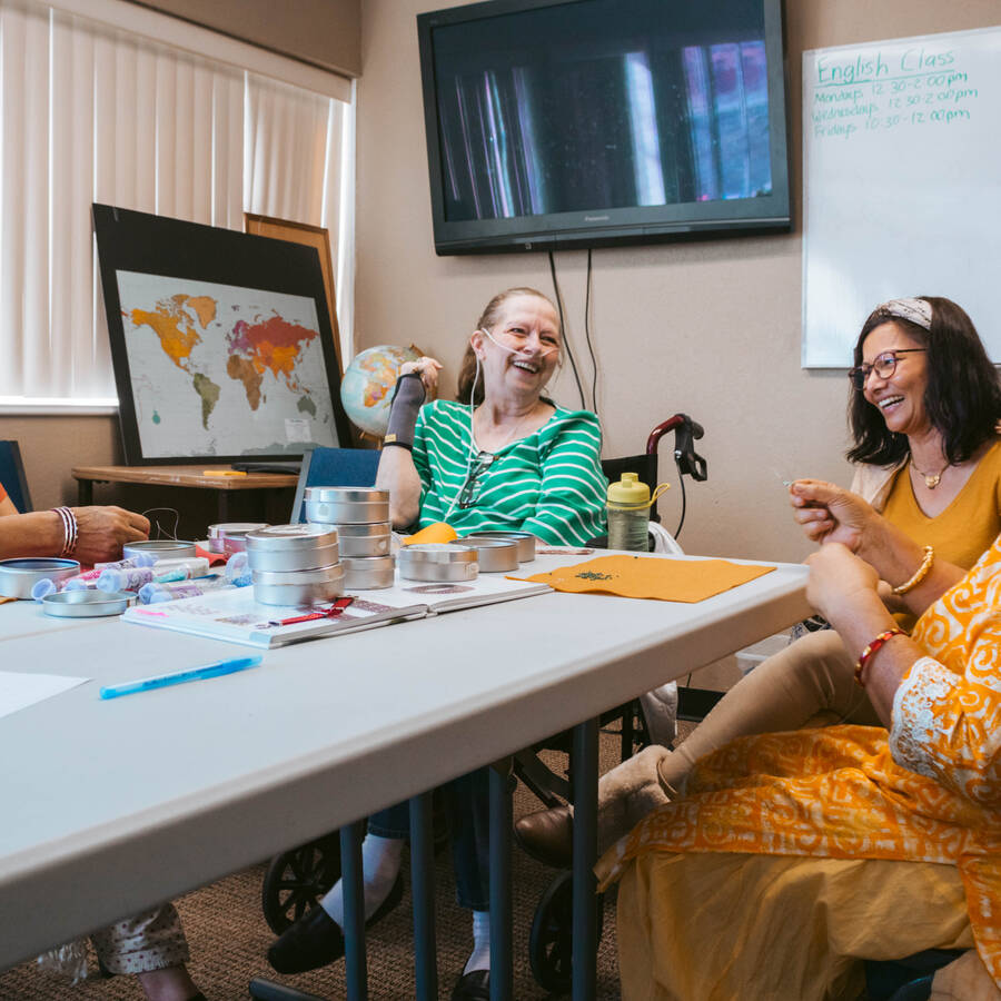 Four individuals are seated around a table in a classroom setting, engaged in a lively discussion with notebooks and cups visible on the table.