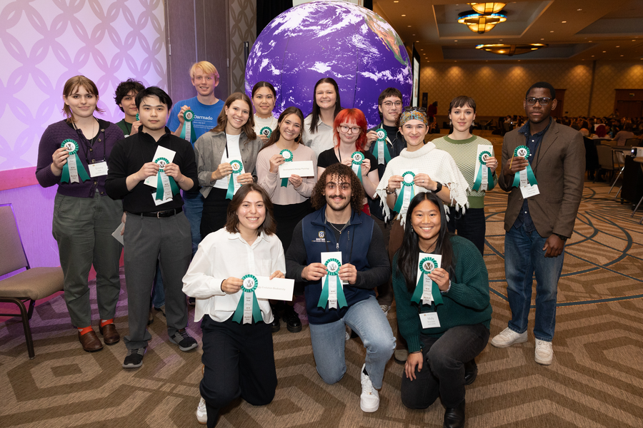 Group of students holding a ribbon and smiling. Some kneeling, others standing behind.